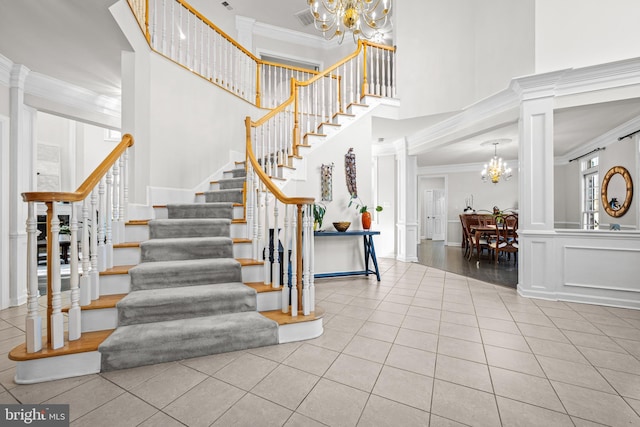 stairway featuring tile patterned floors, visible vents, a notable chandelier, a high ceiling, and crown molding