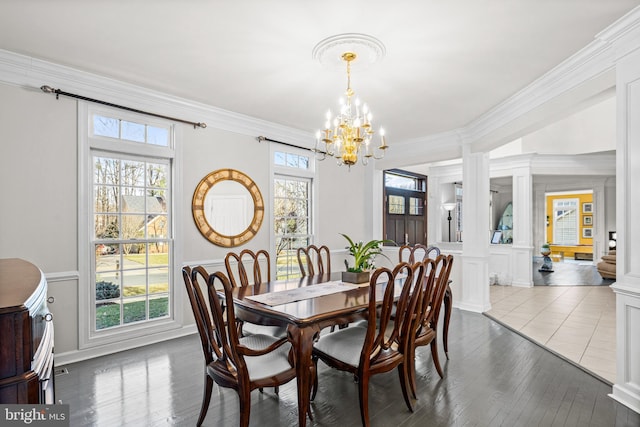 dining space with a decorative wall, ornamental molding, wood finished floors, a notable chandelier, and ornate columns