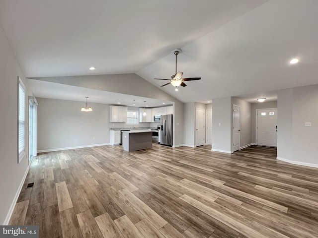 unfurnished living room with light wood-type flooring, visible vents, lofted ceiling, and ceiling fan with notable chandelier