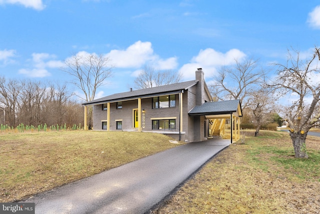 view of front facade featuring driveway, an attached carport, a chimney, and a front yard