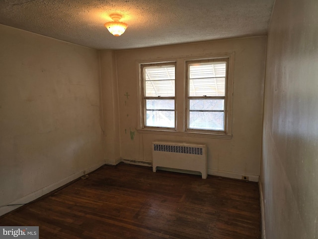 unfurnished room with dark wood-style floors, radiator heating unit, baseboards, and a textured ceiling