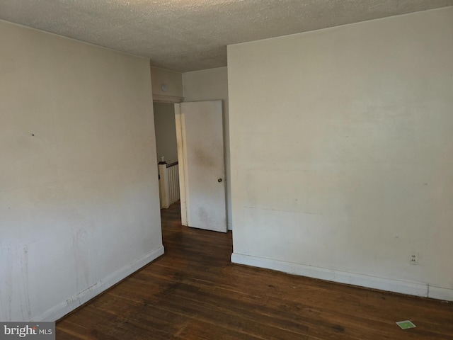 spare room with baseboards, dark wood finished floors, and a textured ceiling