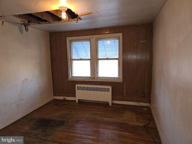 unfurnished room with dark wood-type flooring, baseboards, wood walls, and radiator heating unit