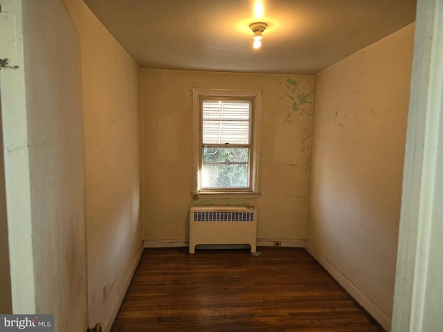 unfurnished room featuring baseboards, dark wood finished floors, and radiator