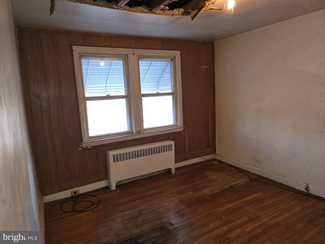 spare room featuring wood walls, radiator heating unit, and dark wood finished floors