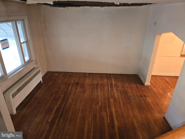 unfurnished room with dark wood-style flooring, radiator heating unit, and baseboards