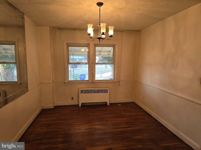 spare room with a textured ceiling, dark wood-style flooring, baseboards, radiator heating unit, and an inviting chandelier