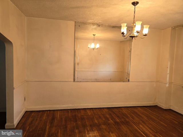 spare room featuring a textured ceiling, baseboards, dark wood finished floors, and an inviting chandelier