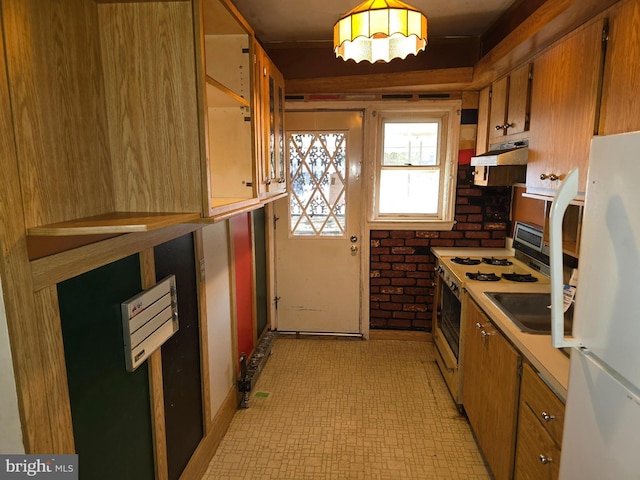 kitchen with under cabinet range hood, brick wall, white appliances, light countertops, and brown cabinets