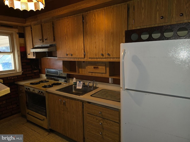 kitchen featuring white appliances, under cabinet range hood, brown cabinetry, and a sink