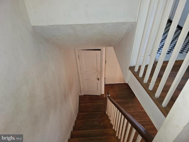 stairway with a textured ceiling and wood finished floors