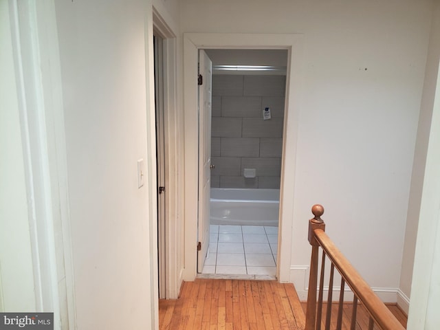 hallway featuring baseboards, an upstairs landing, and light wood-style floors