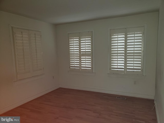 spare room with wood finished floors, visible vents, and baseboards