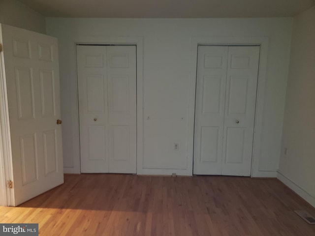 unfurnished bedroom featuring multiple closets, baseboards, visible vents, and wood finished floors