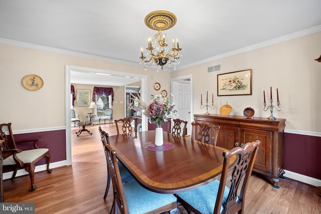 dining area with crown molding, visible vents, a notable chandelier, and light wood-style flooring