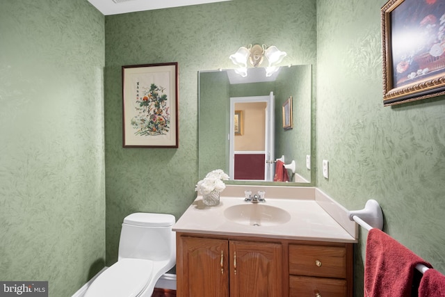 half bath with toilet, vanity, and wallpapered walls