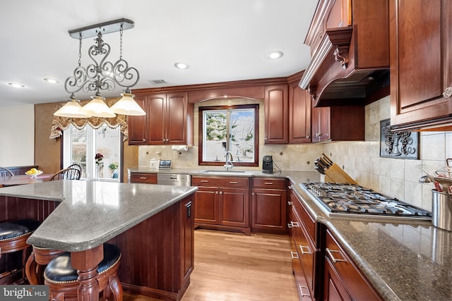 kitchen with pendant lighting, visible vents, light wood-style floors, a sink, and a kitchen breakfast bar