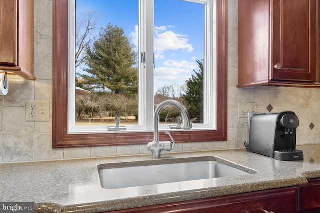 kitchen featuring tasteful backsplash, a sink, light stone counters, and dark brown cabinets