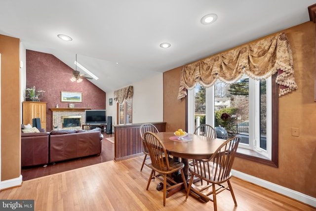 dining space featuring a fireplace, lofted ceiling, light wood-style floors, ceiling fan, and baseboards