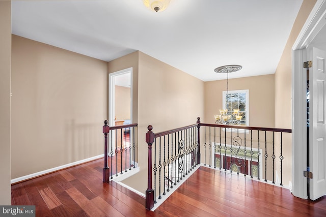 hall with dark wood-style floors, baseboards, an upstairs landing, and a notable chandelier