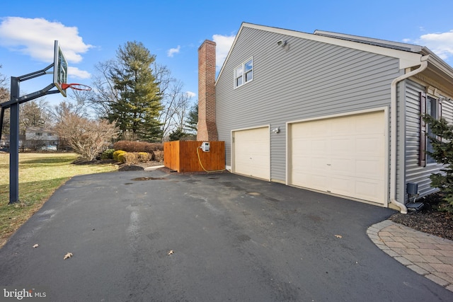 view of side of home with a garage, aphalt driveway, and fence