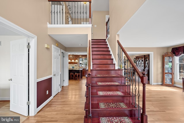 staircase featuring wood finished floors, a towering ceiling, and baseboards