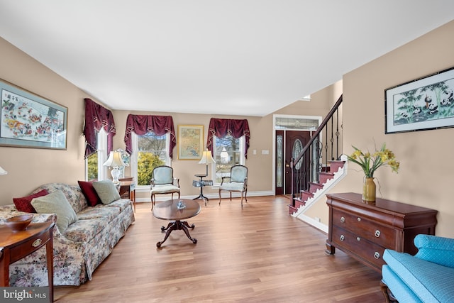 living room featuring light wood-style floors, baseboards, and stairs