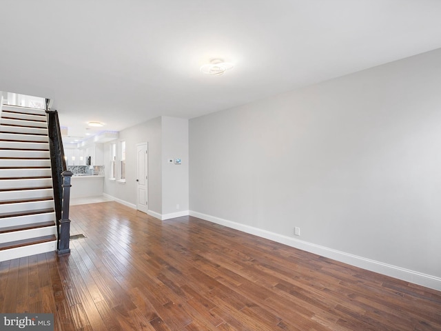 unfurnished living room featuring stairs, dark wood-style flooring, and baseboards