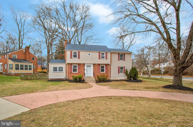 colonial house featuring brick siding, fence, and a front yard