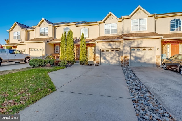 view of property featuring stucco siding, a garage, a residential view, stone siding, and driveway