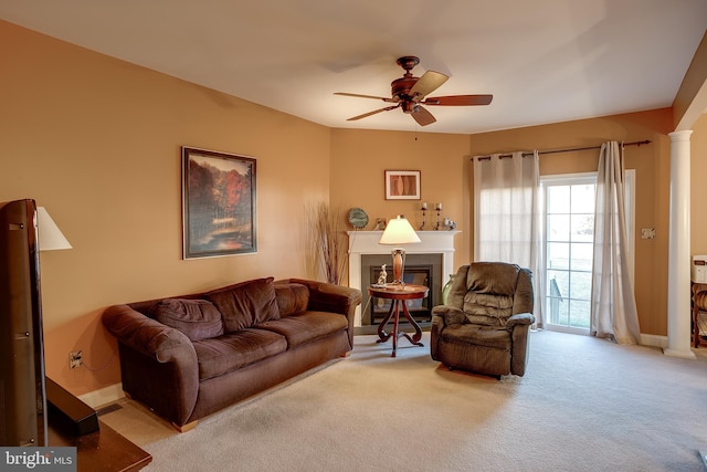 living area with decorative columns, a glass covered fireplace, light carpet, ceiling fan, and baseboards