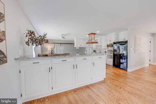 kitchen featuring stainless steel microwave, black fridge with ice dispenser, light wood-style flooring, white cabinetry, and light stone countertops