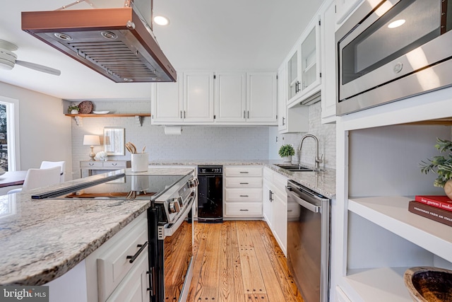 kitchen with stainless steel appliances, white cabinets, a sink, light stone countertops, and exhaust hood