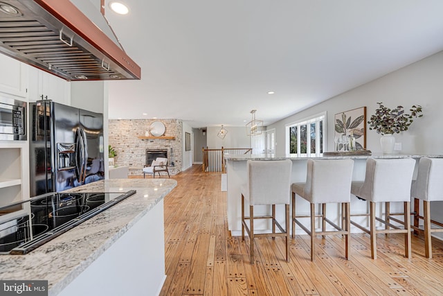 kitchen featuring extractor fan, a breakfast bar area, white cabinets, light wood-type flooring, and black appliances