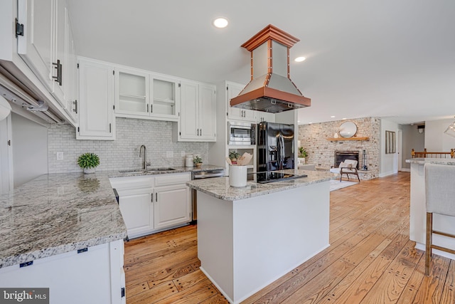 kitchen with light wood finished floors, stainless steel microwave, black fridge with ice dispenser, white cabinets, and a sink