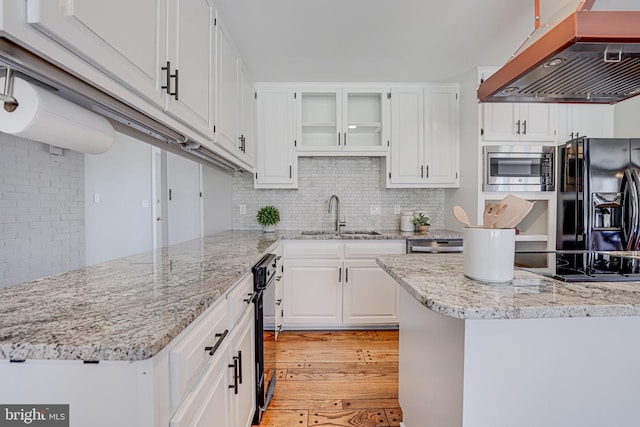 kitchen with under cabinet range hood, a sink, light wood-style floors, white cabinets, and black appliances