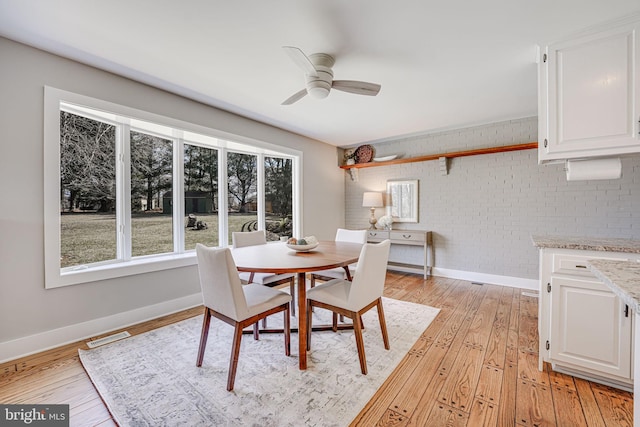 dining room featuring brick wall, light wood finished floors, visible vents, and baseboards