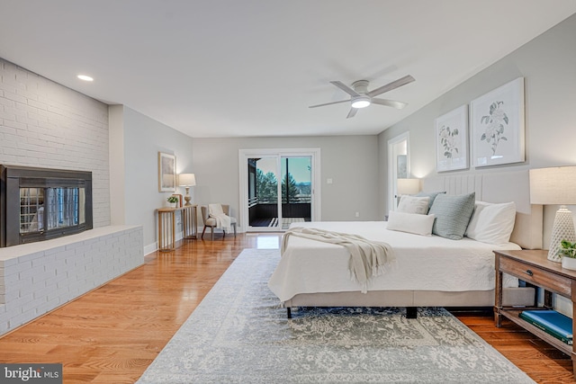 bedroom featuring baseboards, ceiling fan, wood finished floors, access to outside, and a brick fireplace