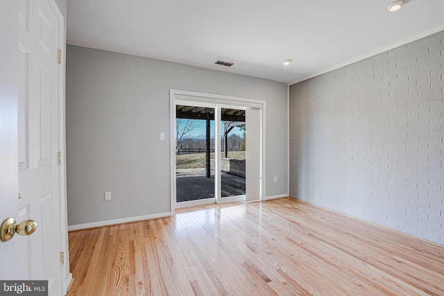 unfurnished room with baseboards, visible vents, light wood finished floors, and brick wall