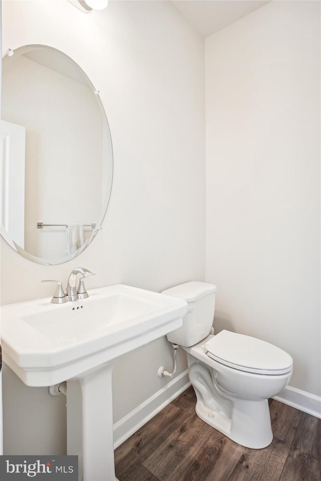 half bath with baseboards, a sink, toilet, and wood finished floors