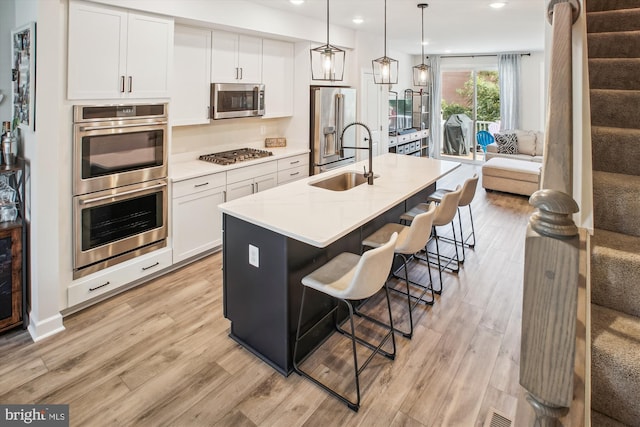 kitchen featuring appliances with stainless steel finishes, white cabinets, a sink, and light wood finished floors