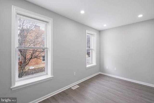 unfurnished room featuring plenty of natural light, visible vents, baseboards, and wood finished floors