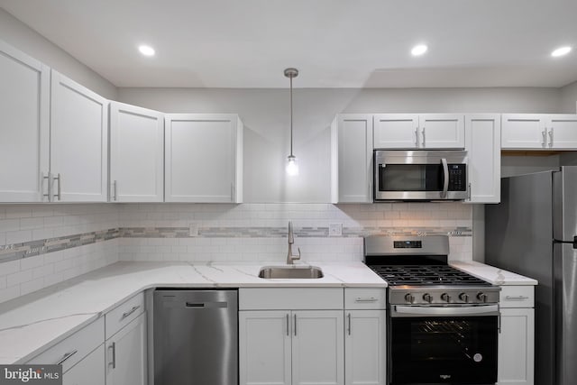 kitchen with decorative light fixtures, appliances with stainless steel finishes, white cabinetry, a sink, and light stone countertops