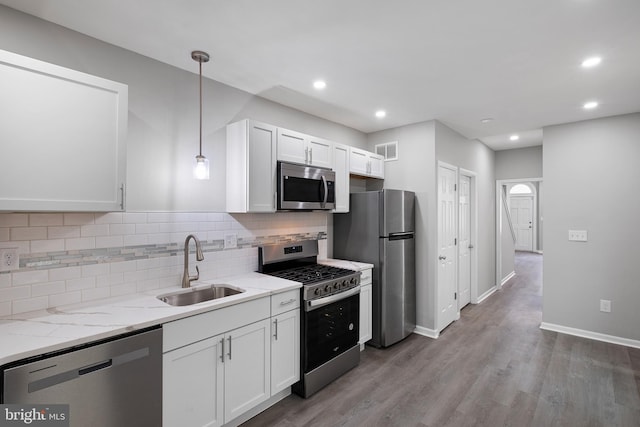 kitchen featuring light stone counters, hanging light fixtures, stainless steel appliances, white cabinetry, and a sink