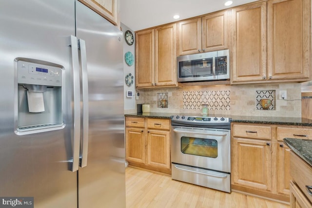 kitchen featuring light wood finished floors, recessed lighting, decorative backsplash, appliances with stainless steel finishes, and dark stone counters