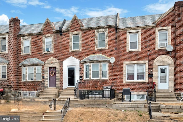 view of property with a high end roof, brick siding, fence, and entry steps