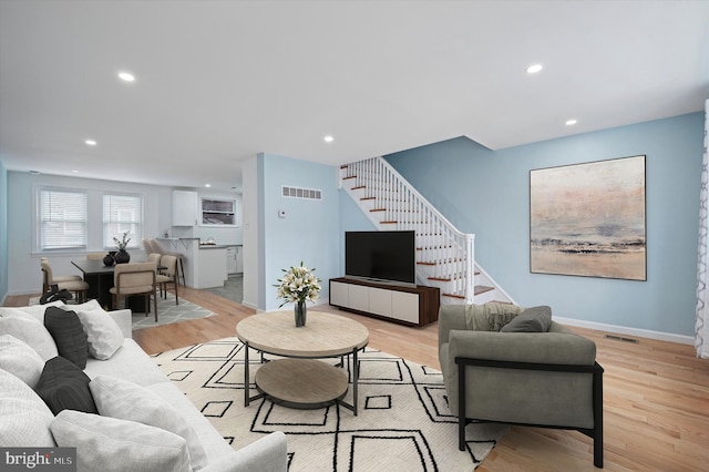 living room with visible vents, light wood-style flooring, and stairs