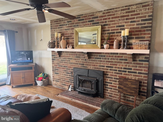 living room with beam ceiling, wood finished floors, a wood stove, and a ceiling fan