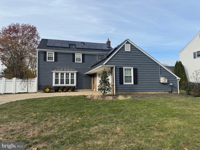 rear view of house featuring solar panels, a lawn, a chimney, and fence