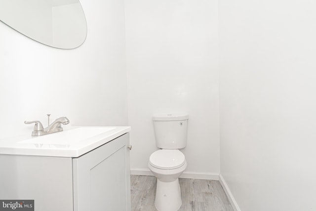 half bath featuring toilet, wood finished floors, vanity, and baseboards